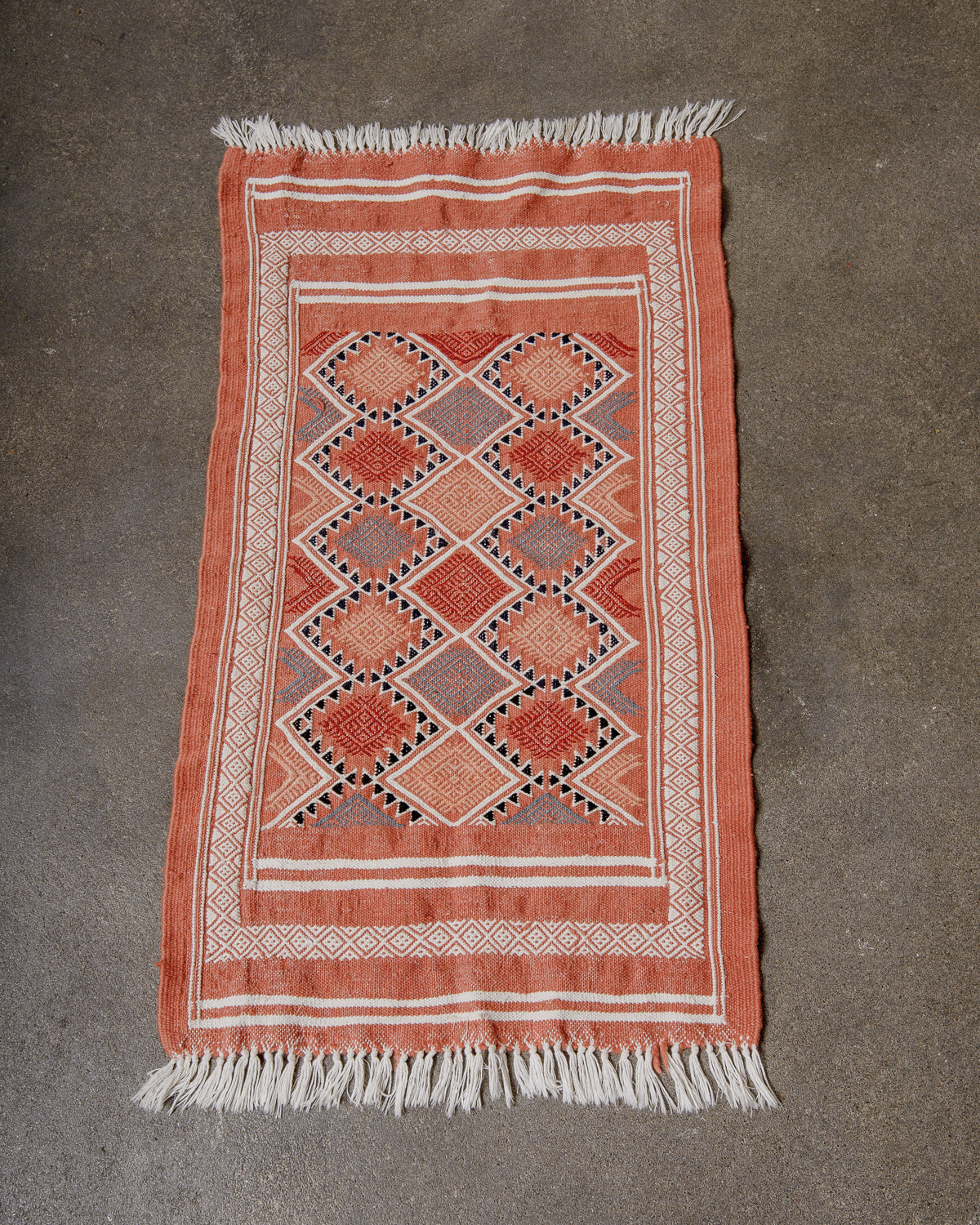 Small Berberlin Vintage Kelim Rug in shades of terracotta and white laying flat on concrete floor.
